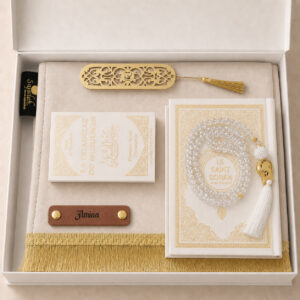Le coffret tapis de prière de couleur blanc Ivoire Sajadah avec ses franges dorées, sa personnalisation en cuir couleur marron, son tasbih effet cristal, son livret "La citadelle du Musulmans" et son Saint Coran de couleur blanc.