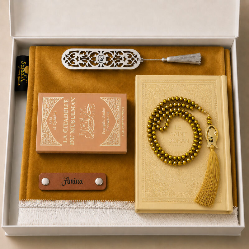 Das personalisierte Sajadah Gebetsteppich-Geschenkset in Honiggelb mit einem Teppich mit weißen Fransen, einem Riemen aus echtem braunem Leder, einem Tasbih in Kristalloptik, einem Exemplar von „Die Festung des Muslims“ und einem Koran.