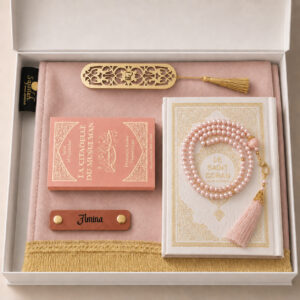 Le coffret tapis de prière de couleur rose Pale Sajadah avec ses franges dorées, sa personnalisation en cuir couleur marron, son tasbih classique, son livret "La citadelle du Musulmans" et son Saint Coran de couleur blanc.