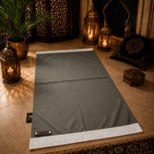 Le tapis de prière personnalisé gris Fer Sajadah avec ses franges blanches et sa lanière en cuir véritable chocolat.