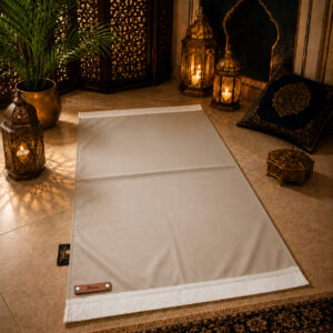 Le tapis de prière personnalisé beige Crème Sajadah avec ses franges blanches et sa lanière en cuir véritable couleur marron.
