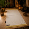 Le tapis de prière personnalisé blanc Ivoire Sajadah avec ses franges dorées et sa lanière en cuir véritable couleur chocolat.
