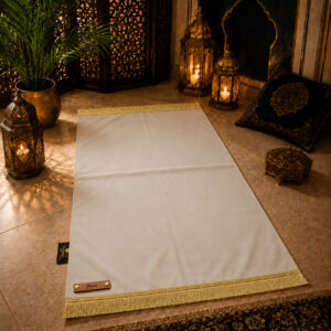 Le tapis de prière personnalisé blanc Ivoire Sajadah avec ses franges dorées et sa lanière en cuir véritable couleur marron.