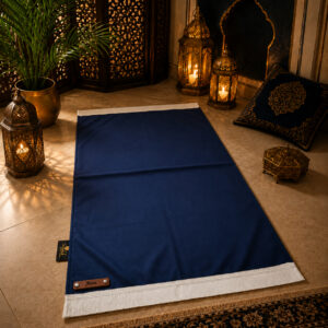 Le tapis de prière personnalisé bleu Nuit Sajadah avec ses franges blanches et sa lanière en cuir véritable marron.