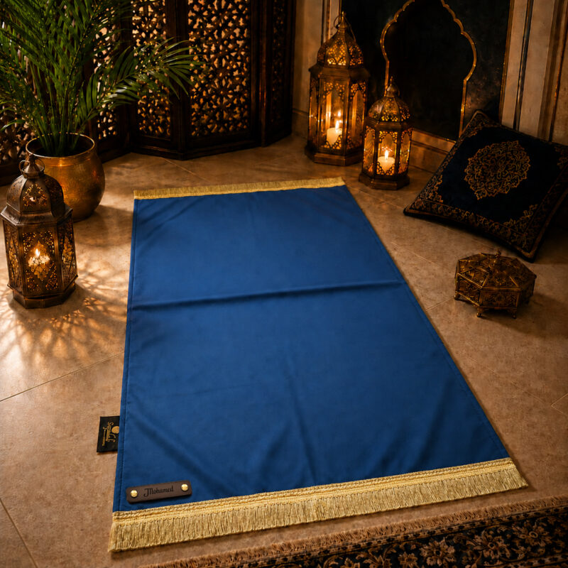 Le tapis de prière personnalisé bleu Roi Sajadah avec ses franges dorées et sa lanière en cuir véritable couleur chocolat.