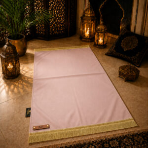 Le tapis de prière personnalisé rose Pâle Sajadah avec ses franges dorées et sa lanière en cuir véritable couleur marron.