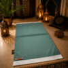 Le tapis de prière personnalisé vert Pin Sajadah avec ses franges blanches et sa lanière en cuir véritable marron.