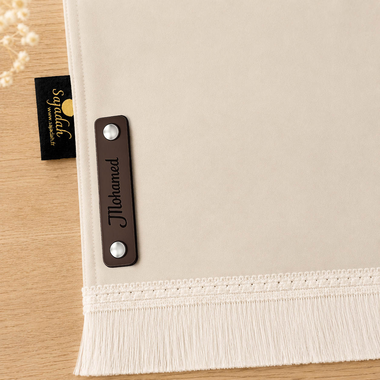 Zoom sur la personnalisation en cuir véritable de couleur chocolat portant votre prénom du tapis de prière Sajadah pour enfant blanc Ivoire.