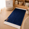 Le tapis de prière Sajadah de couleur bleu Nuit avec ses franges blanches et sa personnalisation en cuir véritable de couleur marron.