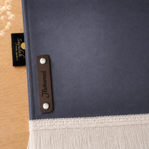 Zoom sur la personnalisation en cuir véritable de couleur chocolat portant votre prénom du tapis de prière Sajadah pour enfant gris Ardoise.