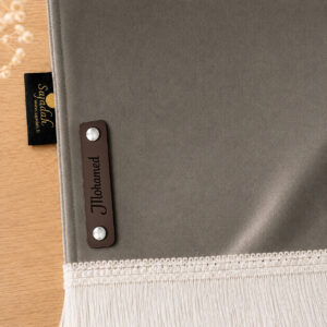 Zoom sur la personnalisation en cuir véritable de couleur chocolat portant votre prénom du tapis de prière Sajadah pour enfant gris Fer.